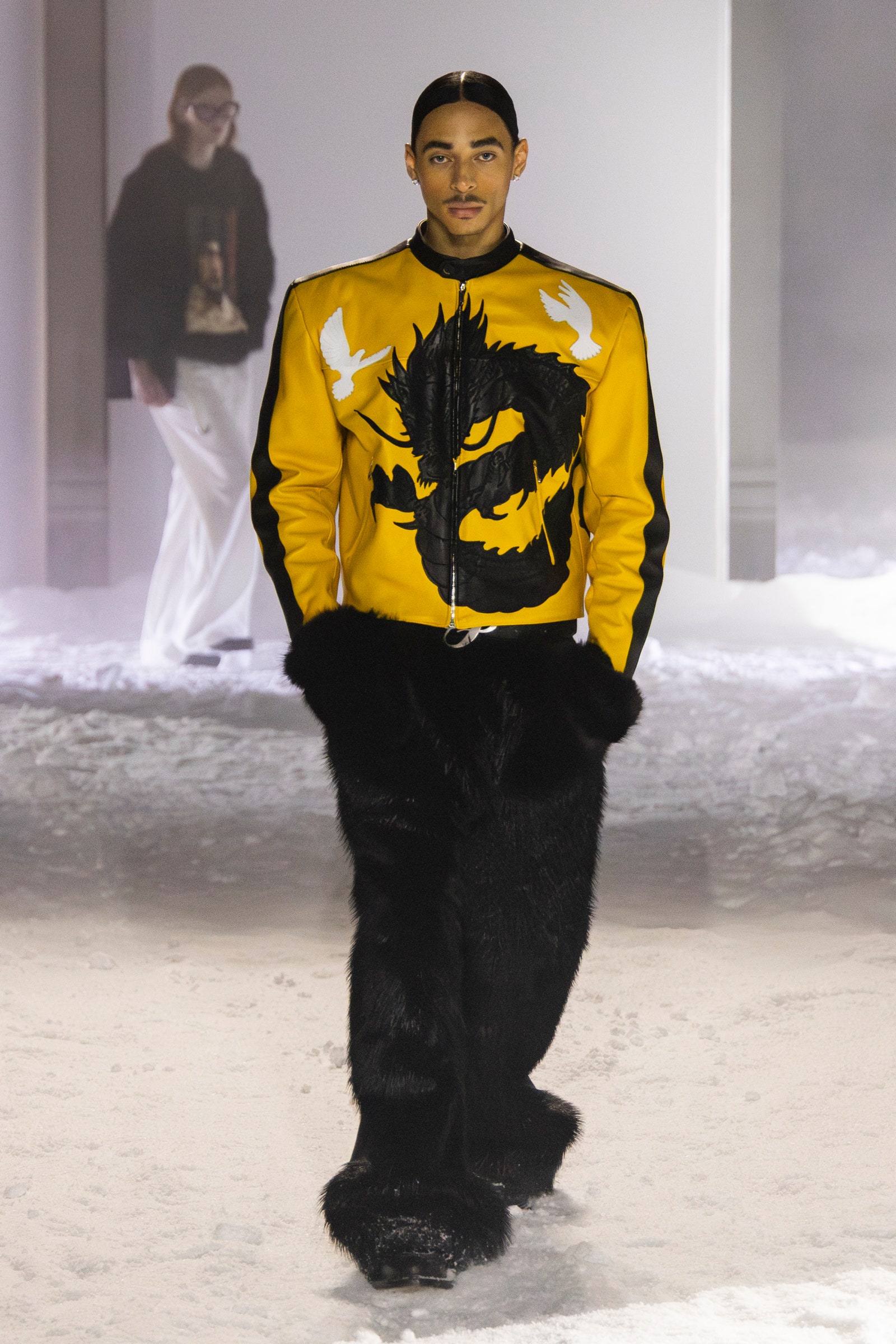 Image may contain Adult Person Clothing Coat Jacket Standing Long Sleeve Sleeve Glove Pants and Accessories